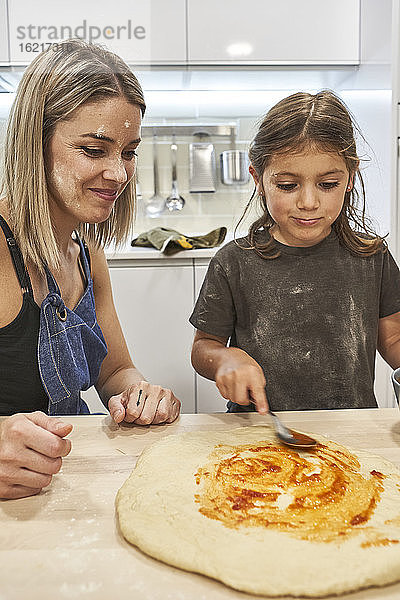 Mutter betrachtet Tochter bei der Zubereitung von Pizza auf dem Tisch in der Küche