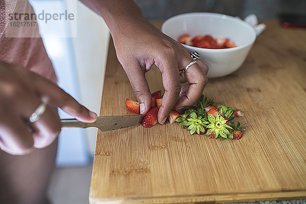 Nahaufnahme einer jungen Frau  die Erdbeeren auf einem Schneidebrett in der Küche zu Hause schneidet