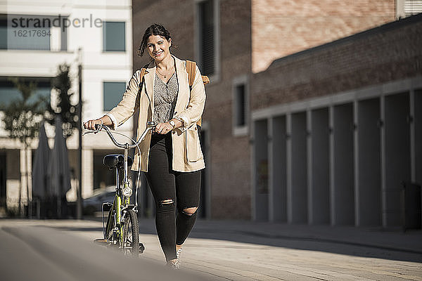 Lächelnder weiblicher Pendler mit Fahrrad auf der Straße in der Stadt