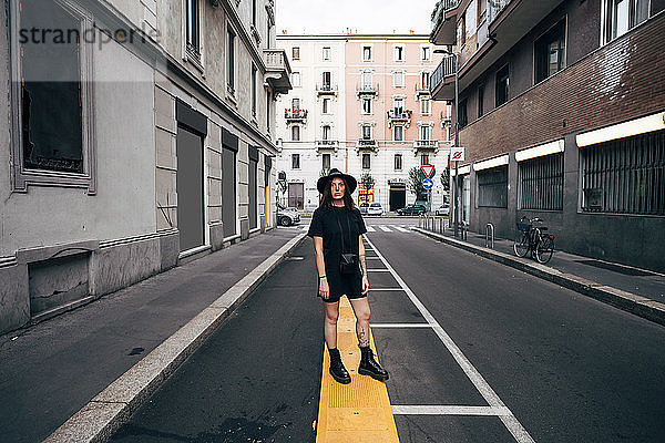 Junge Frau mit Hut steht auf der Straße inmitten von Gebäuden in der Stadt