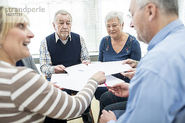 Seniorengruppe  die an einer Therapiegruppe im Altersheim teilnimmt  mit Papierblättern