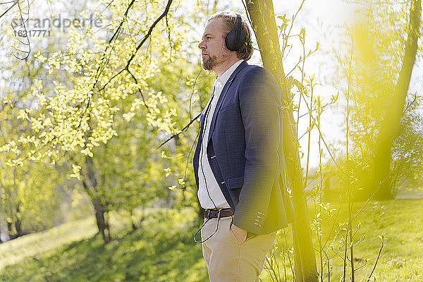 Männlicher Berufstätiger hört Musik  während er an einem sonnigen Tag in den Park blickt