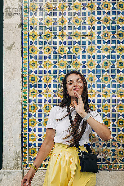 Lächelnde schöne Frau mit langen Haaren  die an einer gekachelten Wand in einer Stadt steht