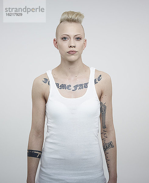 Porträt einer jungen Frau mit Tattoos vor weißem Hintergrund