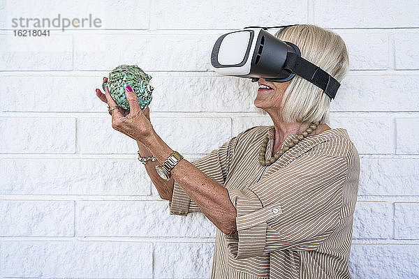 Ältere Frau mit Muschel in der Hand  die einen Virtual-Reality-Simulator benutzt