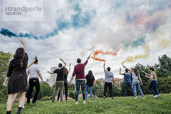 Sorglose Freunde spielen mit Rauchbomben gegen den bewölkten Himmel im Park