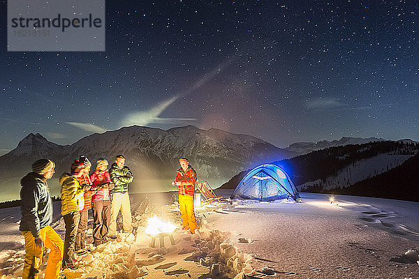 Nachtlandschaft mit glühendem Zelt im Schnee und Menschen am Feuer  Achenkirch  Österreich