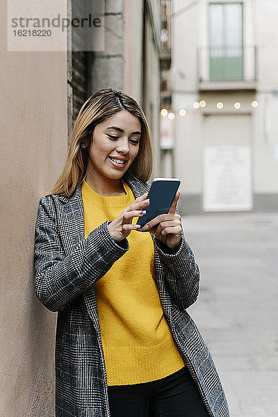 Junge Frau lehnt an der Wand und benutzt ihr Smartphone in der Stadt