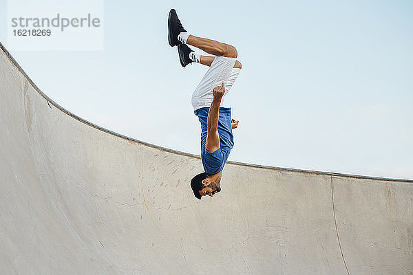 Upside down junger Mann macht Wallflip auf Sport-Rampe gegen Himmel
