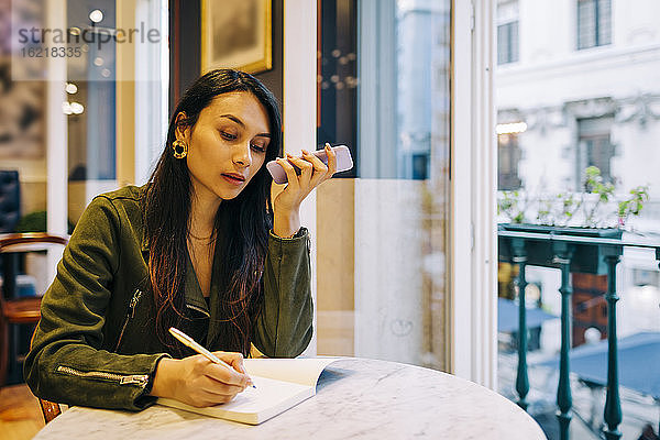 Junge Frau telefoniert in einem Café und schreibt in ein Buch