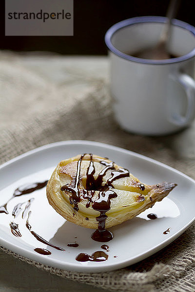 Birne in Blätterteig auf einem Teller mit einem Becher Schokoladensauce  Nahaufnahme