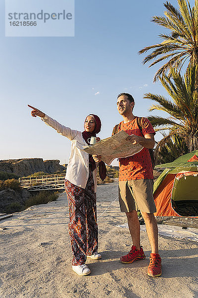 Junge Frau mit Hijab in einem Zelt  die einem Mann mit einer Karte den Weg zeigt