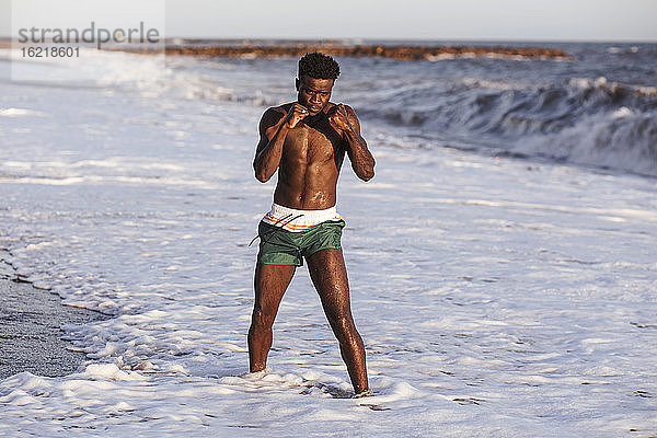 Hemdloser junger Mann beim Sport im Meer stehend