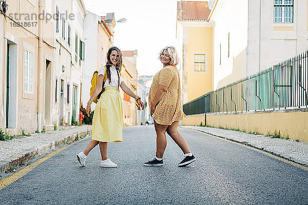 Lächelnde Freunde gehen zusammen auf der Straße in der Stadt