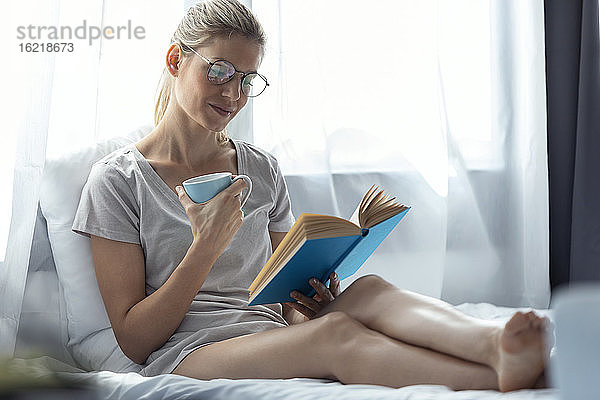 Blonde Frau liest ein Buch im Bett