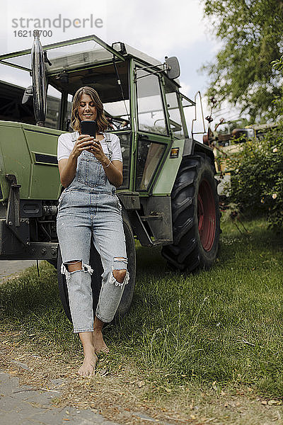 Junge Frau benutzt ein Mobiltelefon an einem Traktor auf dem Lande