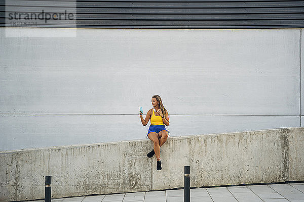 Blonde sportliche Frau macht ein Selfie  sitzt an der Wand