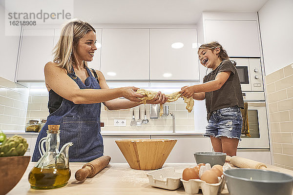 Fröhliche Mutter und Tochter kneten Pizzateig in der Küche zu Hause
