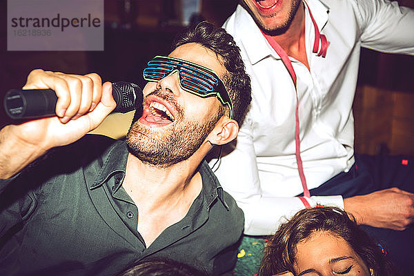 Nahaufnahme eines jungen Mannes  der Karaoke singt und sich mit Freunden auf einer Party amüsiert
