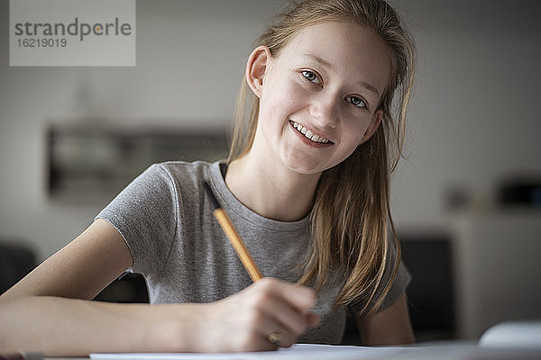 Lächelndes Mädchen  das zu Hause lernt und in ein Schulheft schreibt
