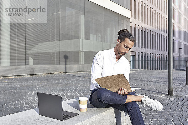 Geschäftsmann liest Akte  während er auf einem Block in der Stadt sitzt