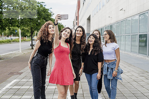 Lächelnde junge Frau  die ein Selfie mit Freundinnen macht  während sie auf einem Fußweg in der Stadt steht