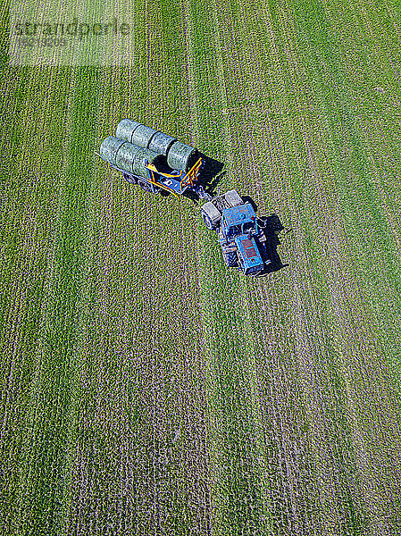 Luftaufnahme eines Traktors  der Heuballen auf einem Feld einsammelt