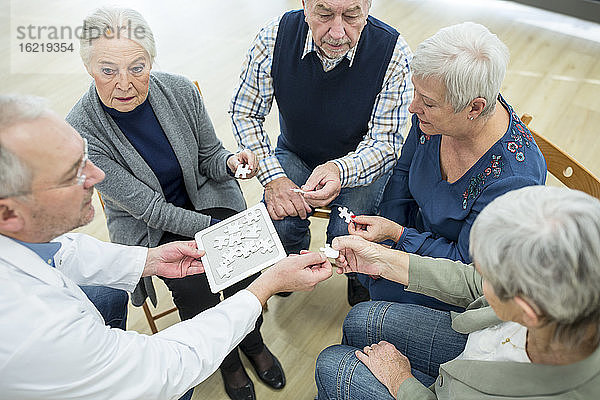 Arzt spielt Puzzle mit einer Gruppe von Senioren im Altersheim