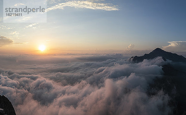 Idyllische Aufnahme eines von Wolken bedeckten Berges bei Sonnenaufgang in den Bergamasker Alpen  Italien