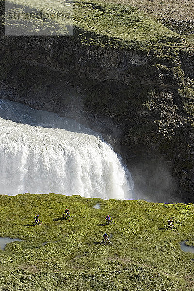 Island  Männer beim Mountainbiking neben einem Wasserfall