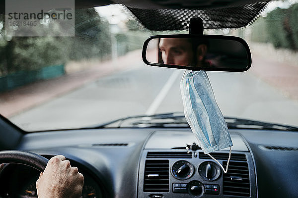 Nahaufnahme einer Gesichtsschutzmaske  die am Rückspiegel eines Autos hängt