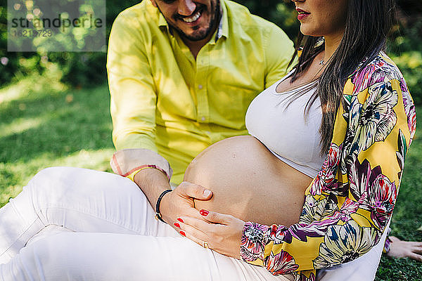 Ehemann berührt den Bauch seiner schwangeren Frau im Park