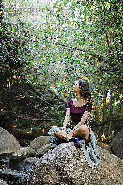 Junge Frau schaut auf einem Stein im Park sitzend nach oben