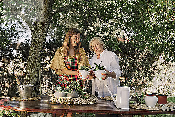 Mutter und Tochter halten Topfpflanzen  während sie an einem Tisch im Garten stehen