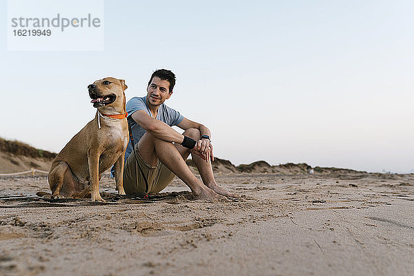 Mann mit seinem Hund am Strand sitzend