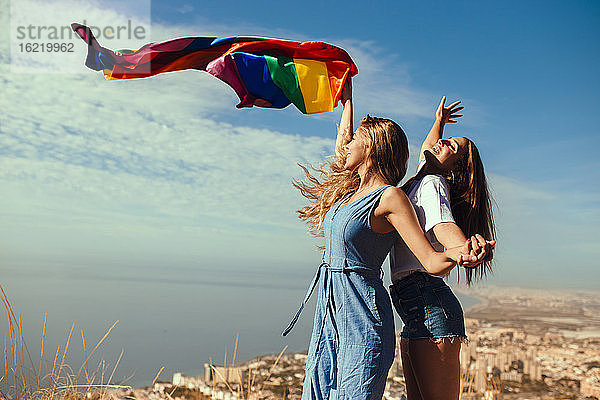 Zwei fröhliche junge Frauen mit einer LGBT-Flagge über der Küstenstadt Almeria  Spanien