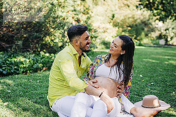Fröhlicher Mann und schwangere Frau verbringen ihre Freizeit zusammen im Park