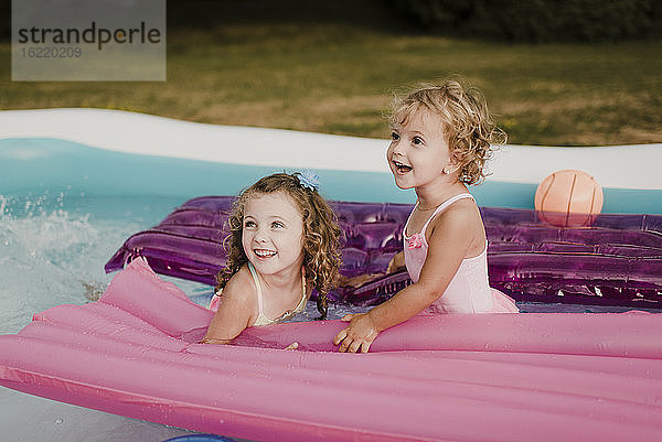 Zwei glückliche Mädchen mit Luftmatratze in einem aufblasbaren Schwimmbad