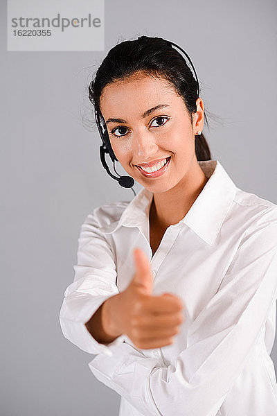 isoliertes Porträt einer fröhlichen jungen brünetten Frau  die als Telefonistin in der Kundenhotline arbeitet  Daumen hoch