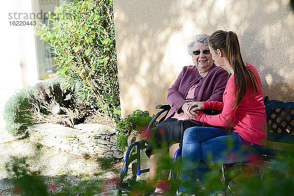 Fröhliche junge Frau im Garten eines Seniorenheims mit einer älteren Dame.