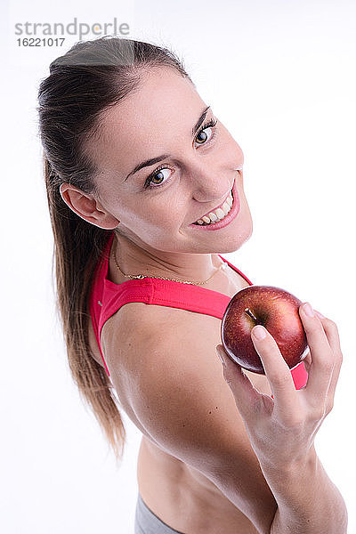 Fröhliche junge kaukasische Frau  die einen roten Apfel isst.