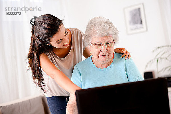 Fröhliche junge Frau  die einer älteren Frau Computer und Internet beibringt