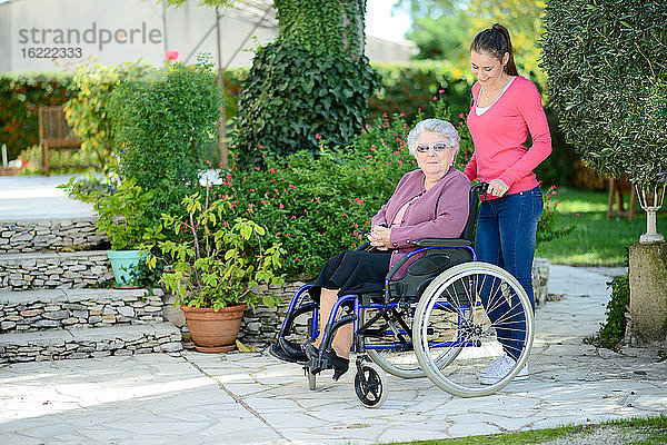 Fröhliche junge Frau im Garten eines Seniorenheims mit einer älteren Dame.