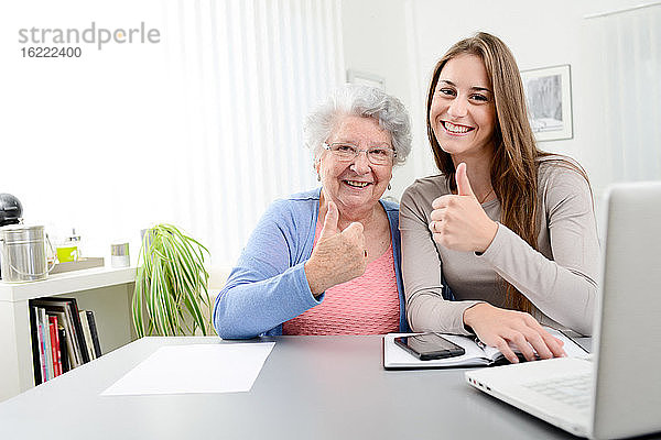 Junge Frau  die einer älteren Frau bei der Erledigung von Papierkram und Verwaltungsverfahren mit einem Laptop zu Hause hilft