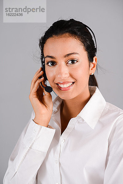 isoliertes Porträt einer fröhlichen jungen brünetten Frau  die als Telefonistin in der Kundenbetreuung arbeitet