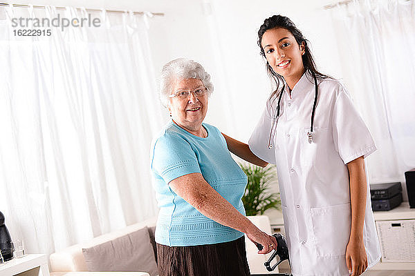 Fröhliche junge Reha-Krankenschwester hilft älterer Frau mit Gehhilfe
