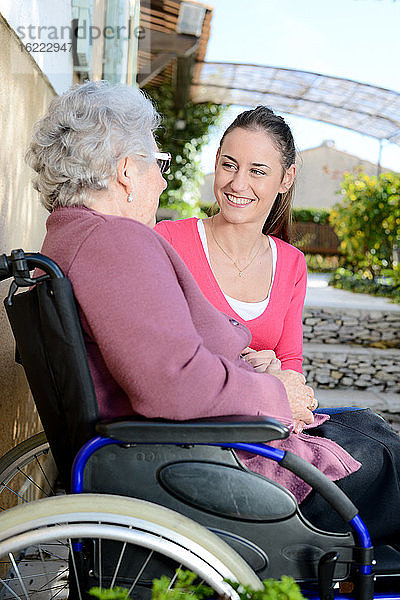 Fröhliche junge Frau im Garten eines Seniorenheims mit einer älteren Dame.