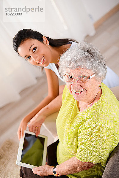 Fröhliches junges Mädchen mit einer älteren Seniorin  die zu Hause mit einem digitalen Tablet spielt