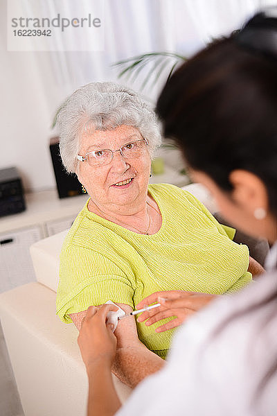 Fröhliche junge Krankenschwester gibt einer älteren Frau zu Hause eine Spritze