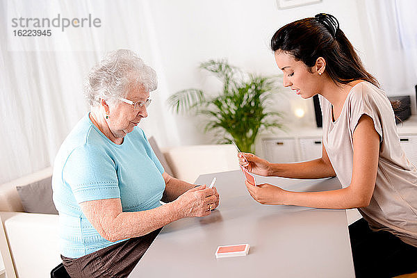 Fröhliches junges Mädchen spielt Karten mit älterer Seniorin